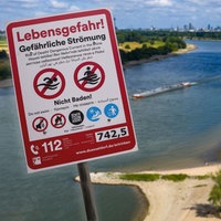 Montage: Schild zum Badeverbot, dahinter Luftbild vom Rhein 