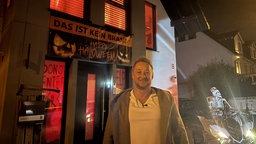 Ein blonder Mann steht vor seinem Halloween-Haus. Er hat es so geschmückt, dass es so wirkt als würde es brennen. Ein Schock zu Halloween.