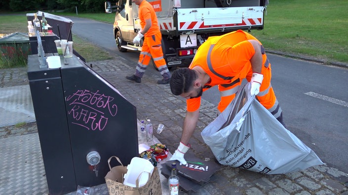 Zwei Männer räumen Müll um eine Mülltonne weg
