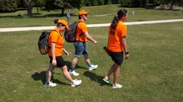 Drei Frauen in orangen T-Shirts gehen durch einen Park
