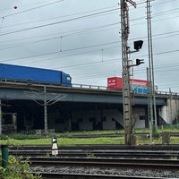 Seitenansicht auf die Brücke, auf der LKWs stehen und darunter Schienen verlaufen 