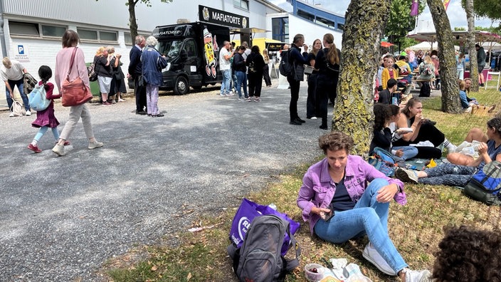Menschen sitzen auf Rand von Wiese und machen Picknick