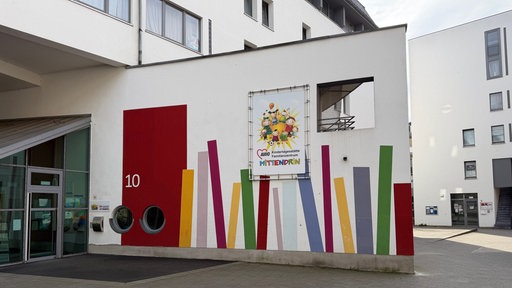 Bunte Wand am Eingang einer Kindertagesstätte. Daran hängt ein AWO-Mittendrin Plakat.