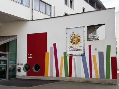 Bunte Wand am Eingang einer Kindertagesstätte. Daran hängt ein AWO-Mittendrin Plakat.