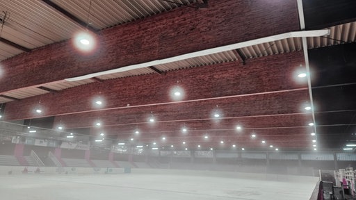Eine leere Eisfläche in einer Halle. Über dem Eisfeld liegt Nebel.