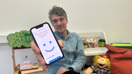 Ein Mann hält ein Smartphone in die Kamera mit einer geöffneten App, die eine Frage stellt