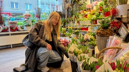 Eine Frau hockt in einem Blumenladen vor einer Auswahl an Pflanzen