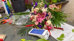 Ein EC-Bezahlgerät liegt auf einem Tisch voller Blumen