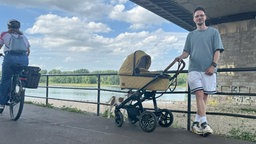 Vater mit Kinderwagen und Hund steht auf von Rädern viel befahrenem Weg am Rhein unter der Brücke.