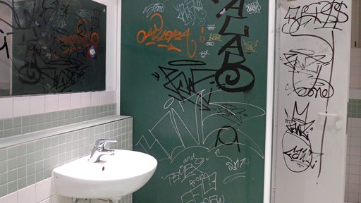 Eine Schultoilette, deren Wände mit Graffiti beschmiert sind.