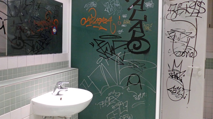 Eine Schultoilette, deren Wände mit Graffiti beschmiert sind.