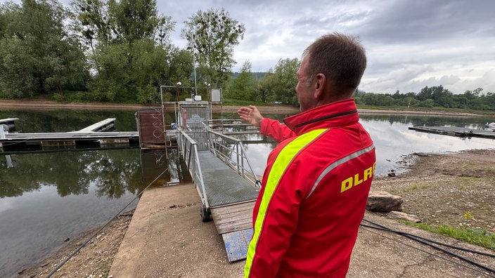 Mann (DLRG) deutet auf Bootsanleger.