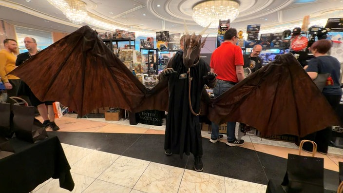 Person im Kostüm des Drachen Cupro mit schwarzem Umhang und riesigen Flügeln