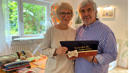 Ehepaar Blum steht in ihrem Wohnzimmer mit einem dunklen Krätzchen in der Hand