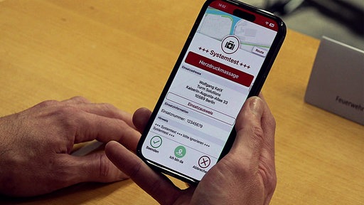 Auf einem dunklen Handy wird eine Notfallapp von "KatRetter" dargestellt. Das Handy wird von zwei Händen gehalten.