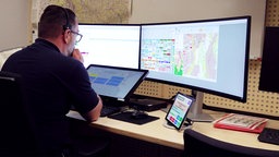 Ein Mann schaut auf drei Computerbildschirme. Auf den Bildschirmen ist die Karte für Notfälle der "KatRetter-App" dargestellt.