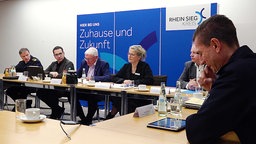 Eine Pressekonferenz von sechs Personen, mit einer blauen Werbetafel im Hintergrund, mit der Aufschrift "Zuhause und Zukunft."