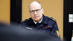 Ulrich Heister, Ärztlicher Leiter des Bonner Rettungsdienstes, ein Mann mit grauen Haaren und schmaler, schwarzer Brille, trägt eine blaue Feuerwehr-Uniform und sitzt vor einer holzvertäfelten Wand.