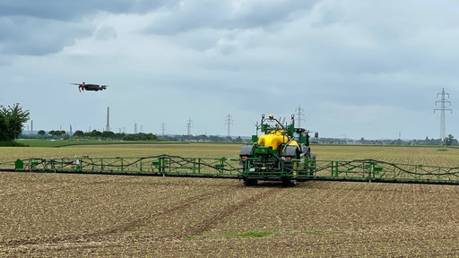 Landwirtschaftliche Maschine auf einem Feld, daneben schwebt eine Drohne.