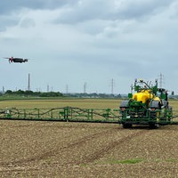 Landwirtschaftliche Maschine auf einem Feld, daneben schwebt eine Drohne.