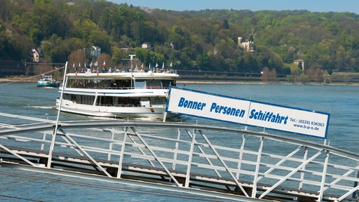 Ein Schiff fährt auf einen Steg zu, auf dem in blauer Schrift "Bonner Personen Schiffahrt" steht.