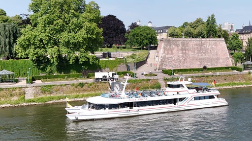 Ein weißes Schiff liegt an einem Flussufer an.