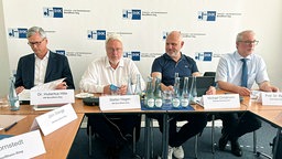 Vier Männer in Hemden sitzen hinter einem Tisch, vor ihnen Namensschilder. Im Hintergrund ein Werbeaufsteller der Industrie- und Handelskammer Bonn/Rhein-Sieg.