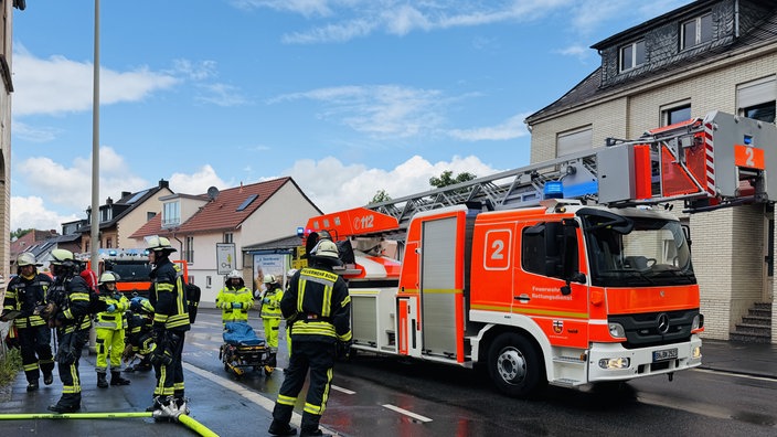 Feuerwehrleute in Einsatzkleidung vor einem Feuerwehrauto mit eingeklappter Leiter
