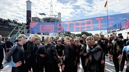 Sportler stehen mit Badekappe und Neoprenanzug am Startpunkt des Bonner Triathlons