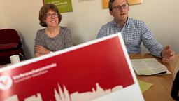 Frau und Mann sitzen nebeneinander und vor den Beiden ist ein Hinweiszettel von der Verbraucherzentrale