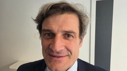 Ein mittelalter Mann mit etwas krausem Haar mit gestreiftem Hemd, Krawatte und Anzug