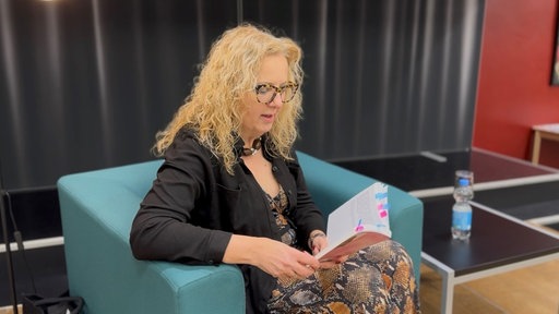 Eine Frau auf einer Bühne, sie hält ein Buch in der Hand.