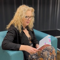 Eine Frau auf einer Bühne, sie hält ein Buch in der Hand.