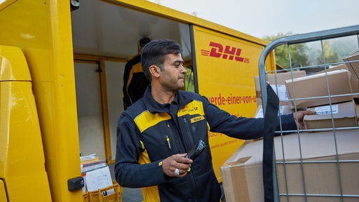 Ein Geflüchter, der mittlerweile bei DHL in der Zustellung arbeitet, vor einem DHL-Zustellfahrzeug.
