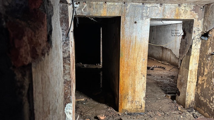 Zwei verlassene Räume eines Bunkers. Man sieht verwitterte Wände und einen schlammbedeckten Boden.