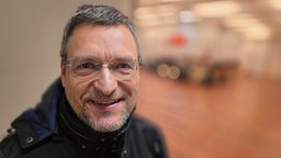EIn Mann mit durchsichtiger Brille, Bart und grauem Haar in einem Saaleingang