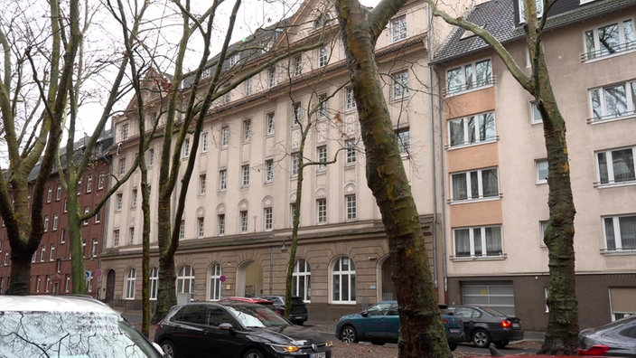 Eine breite Häuserfront von der Straße aus, davor Bäume