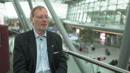 Ein Mann mit Brille sitzt in der Empfangshalle des Düsseldorfer Flughafens. 