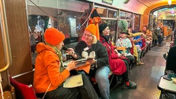 Zwei Frauen, die als Kürbis verkleidet sind, sitzen in einer Bahn.