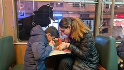 Mutter und Sohn sind über ein Blatt Papier gebeugt und sitzen in einer Bahn