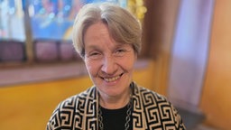 Eine Frau lächelt in die Kamera, im Hintergrund sieht man gelbe Wände