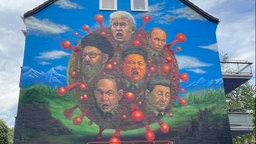 Auf dem Foto ist ein rundes Virus-Symbol, darauf die Gesichter von Donald Trump, Xi Jinping, Benjamin Netanjahu, Wladimir Putin und Ali Chamenei.