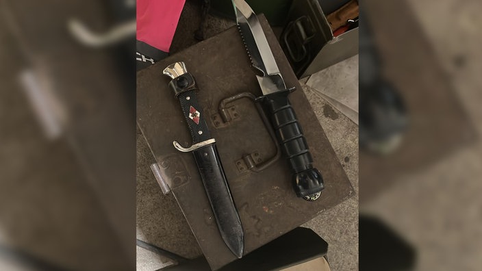 Zwei Messer liegen auf einer Kiste. Eines davon im Holster. 