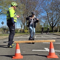 Jugendliche auf E-Scooter fährt auf ein Hindernis zu, Polizist steht daneben
