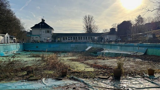 Mirker Freibad von Außen, im Vordergrund das leere verwilderte Schwimmbecken, bei Sonnenaufgang