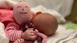 Ein Baby in einem Strampler mit Stoffpuppe
