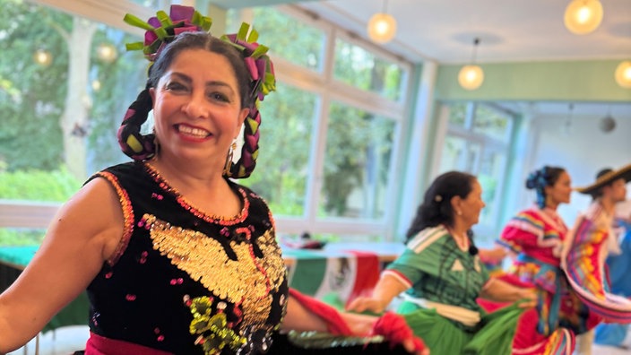 Die Tänzerin Judith Reyes des Spiss aus der Tanzgruppe Viva México tanzt in farbrohem Gewand zusammen mit anderen Tänzerinnen der Tanzgruppe.