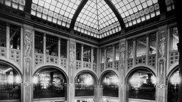 Eine Schwarz-Weiß-Ansichtskarte, die ein großes Kaufhaus von innen mit großer Glaskuppel zeigt