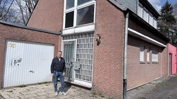 Gerrit Hermes, ein Mann mittleren Alters in Jeans und dunkler Jacke, steht vor eine Backsteinhaus