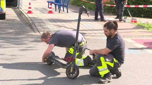 Zwei Männer von der Unfallaufnahme untersuchen auf der Straße einen E-Scooter